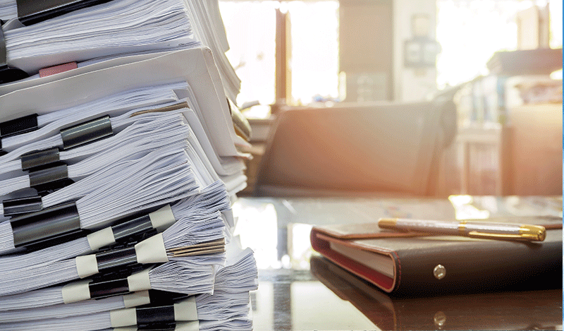 A stack of regulations in paper form sit on the desk of a bureaucrat