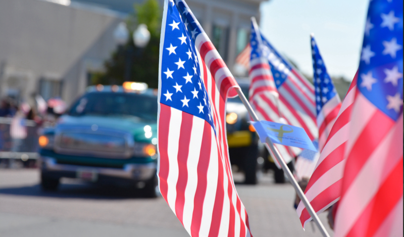 American Flags are seen with a Veterans Day parade passing in the background